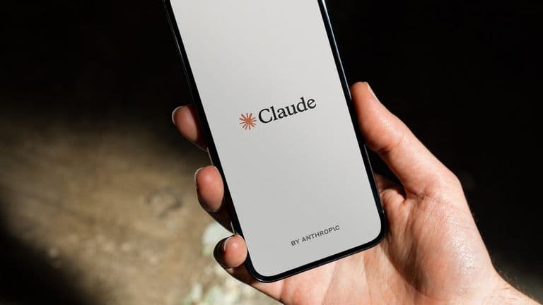Käsi pitelee puhelinta, jonka näytöllä on Clauden logo ja teksti By Anthropic