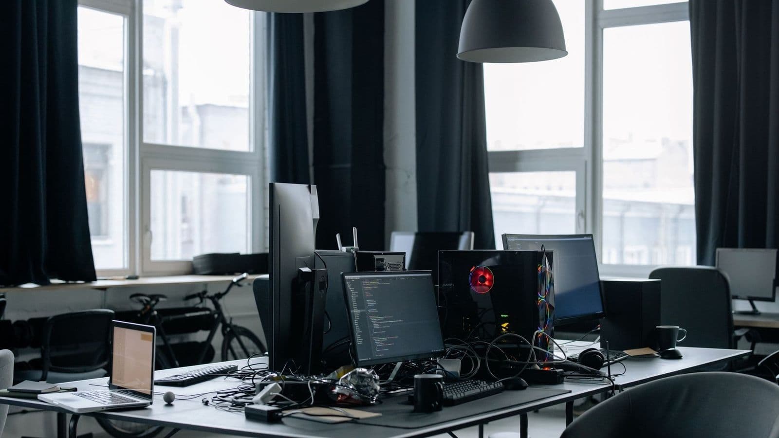 Ohjelmistokehittäjän työpöytä, jolla on useita näyttöjä koodineditorin kanssa, tietokone ja kannettava tilavassa toimistossa.