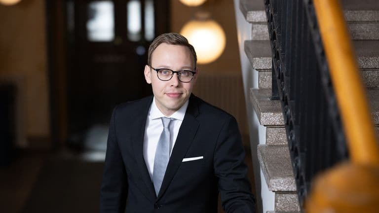 Työministeri Matias Marttinen tummassa puvussa ja silmälasit päässä portaikossa.