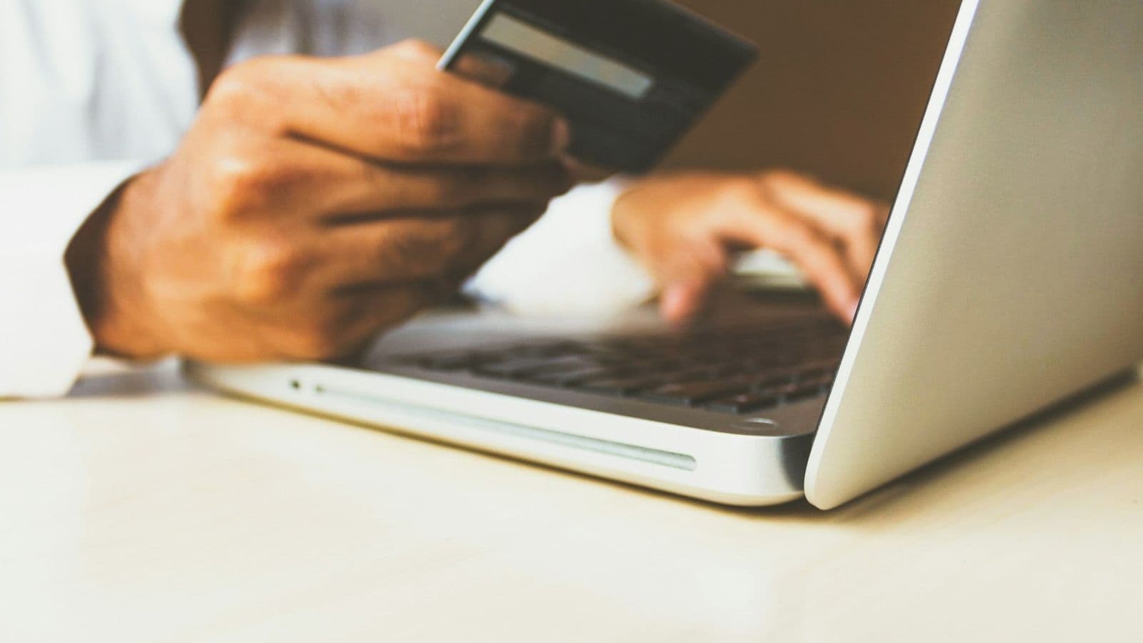 Henkilö pitää pankkikorttia kädessään ja kirjoittaa kannettavalla tietokoneella verkkomaksun yhteydessä