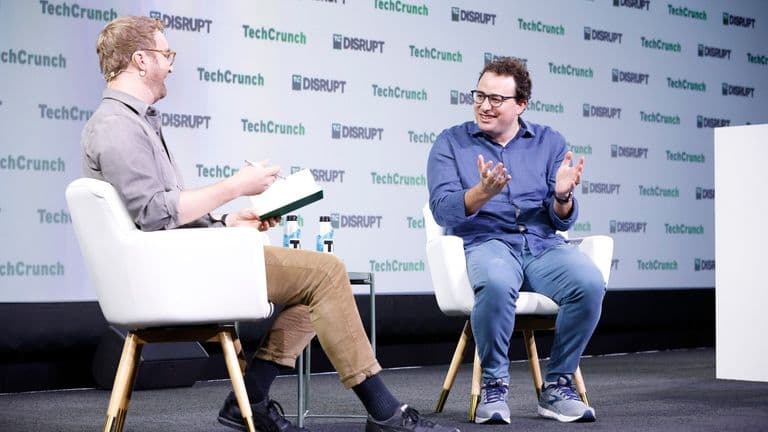 Dario Amodei puhuu ja elehtii haastattelijan vastapäätä TechCrunch Disrupt -tapahtuman lavalla