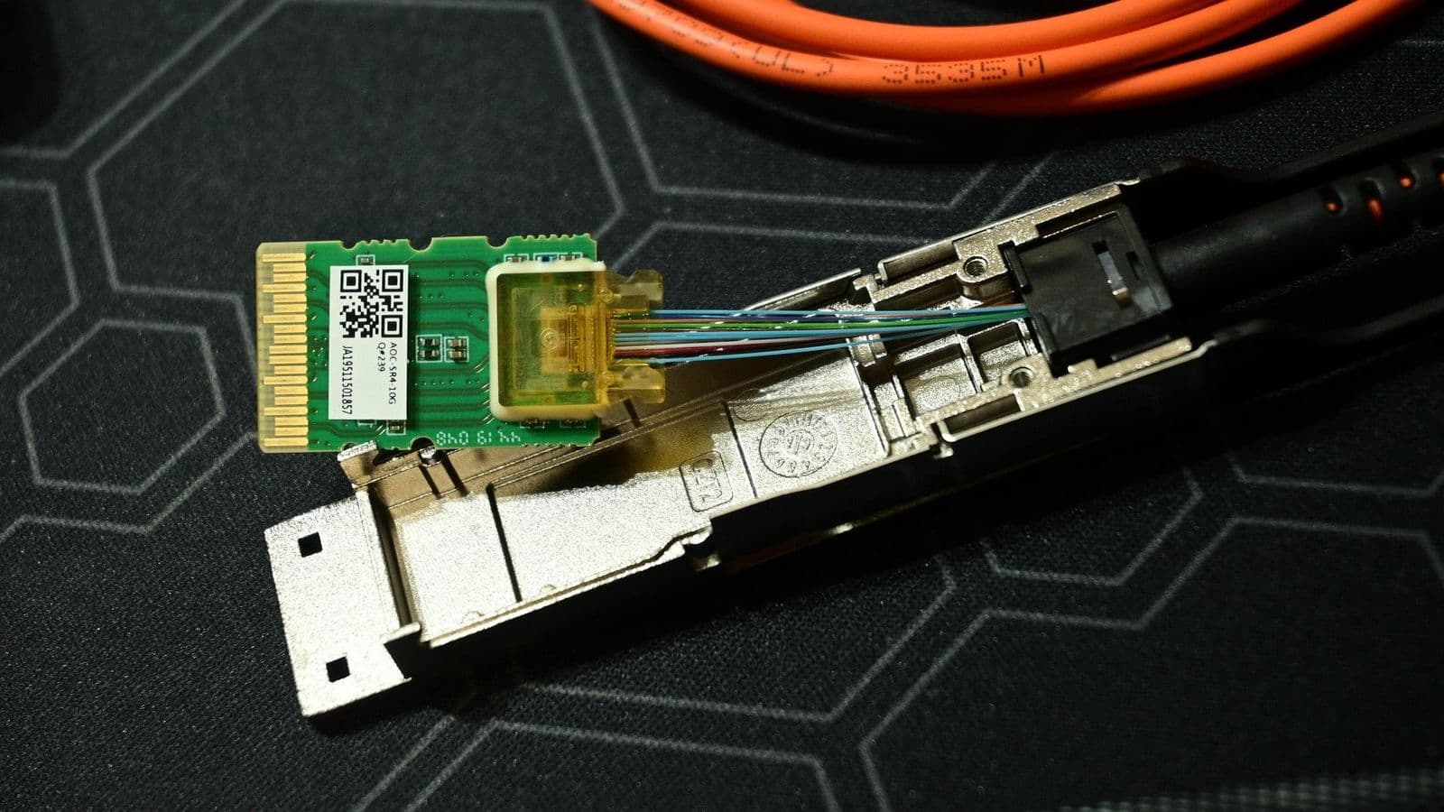 Purettu QSFP-optinen lähetin-vastaanotin, jonka piirilevy ja valokuidut näkyvät oranssin kaapelin vieressä.