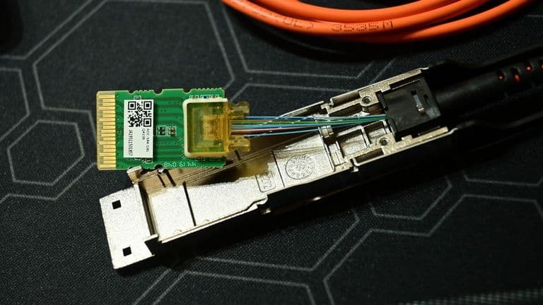Purettu QSFP-optinen lähetin-vastaanotin, jonka piirilevy ja valokuidut näkyvät oranssin kaapelin vieressä.