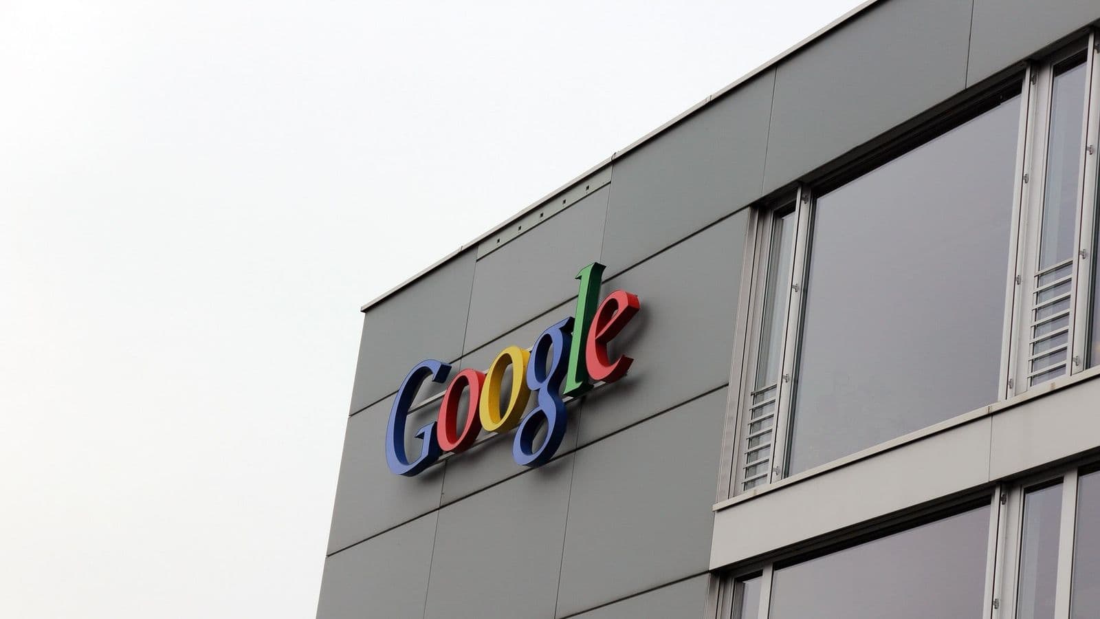 Googlen värikäs logo harmaan toimistorakennuksen seinässä pilvisen taivaan alla